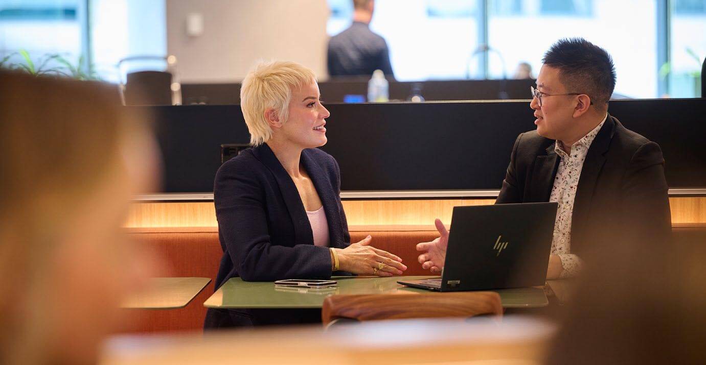 Two people sitting at a table in an office having a meeting around a computer 